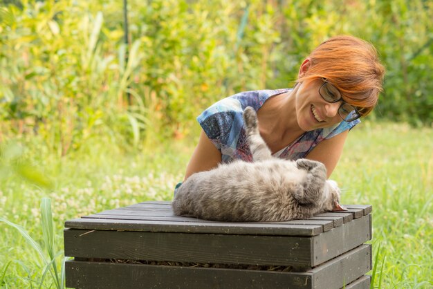 Женщина играет с кошкой на открытом воздухе в зеленом саду дома