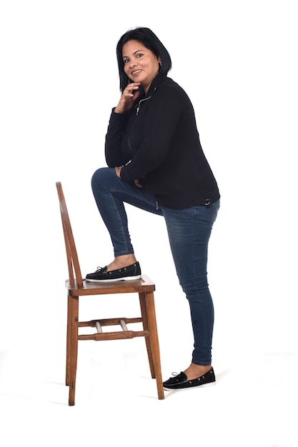 Woman playing with a chair in white background, hand on chin and foot on the chair