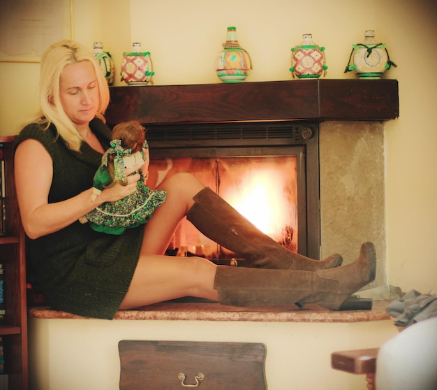 Женщина играет с куклой, сидя рядом с огнем дома
