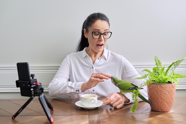 Woman playing with her pet parrot at home bird biting woman's finger