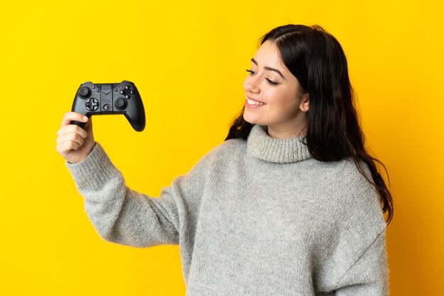 Woman playing with a video game controllerisolrted on yellow wall with happy expression