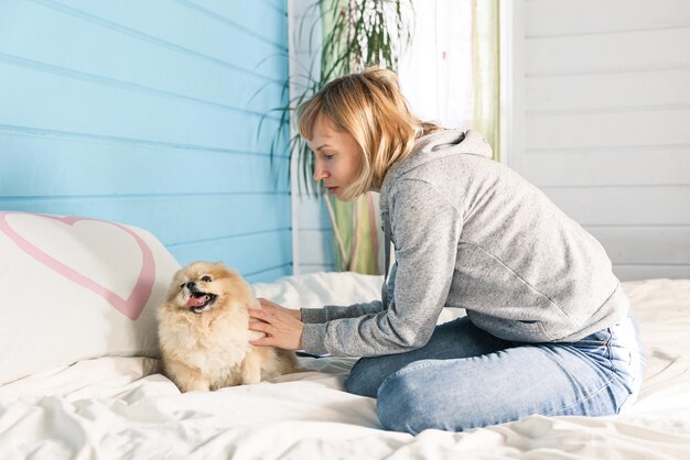 Woman plays with dog on bed in bedroom
