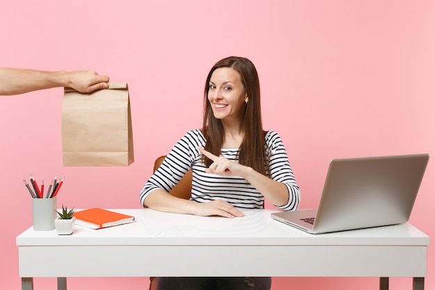 Женщина, указывая на коричневый чистый пустой пустой бумажный пакет ремесла, работа в офисе с ноутбуком