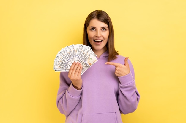 Woman pointing at dollar banknotes in her hand having positive expression big profit