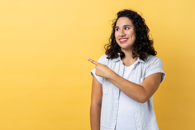 Woman pointing finger away with toothy smile wondering about empty space for your advertisement