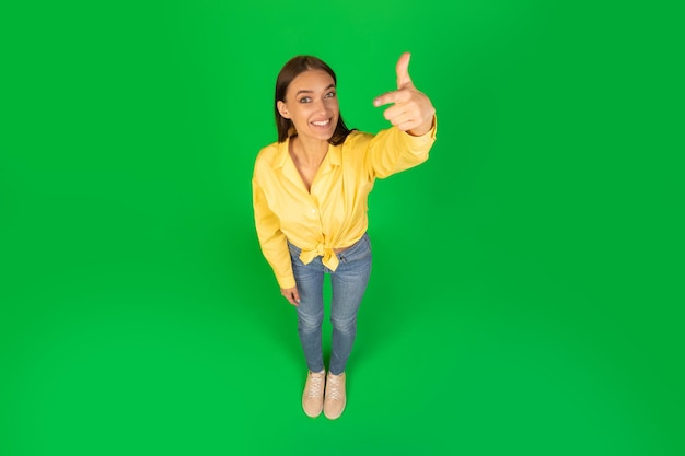 Woman pointing finger at camera over green background high angle