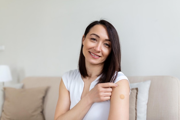 Woman pointing at her arm with a bandage after receiving the covid19 vaccine Asian woman showing her shoulder after getting coronavirus vaccine