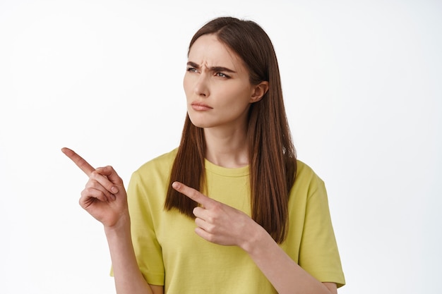 woman pointing, looking left at smth strange, what is that expression, cant understand, standing puzzled on white.