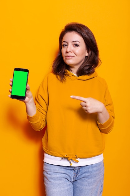 Woman pointing at smartphone with vertical green screen