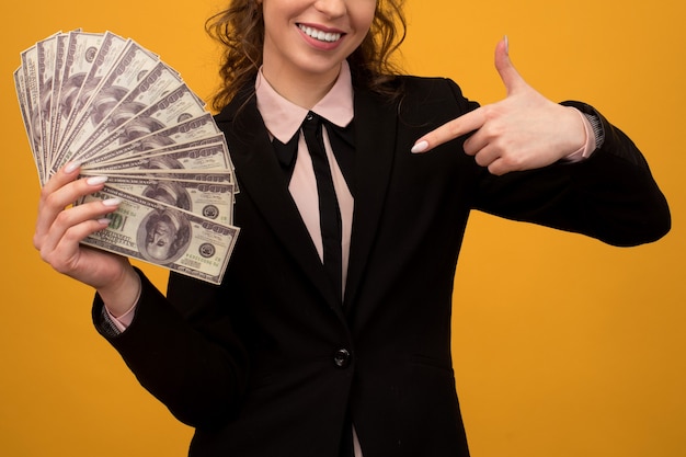 Женщина, указывая на стопку денег пальцем, изолированным на желтом фоне.