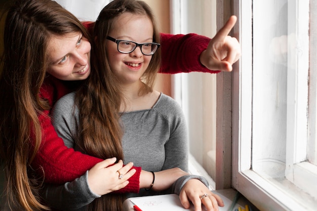 Photo woman pointing at window to girl with down syndrome