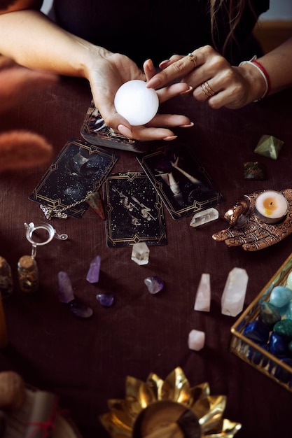 A woman points to a crystal ball that she holds in her hand as
she does a tarot card reading on her witch altar