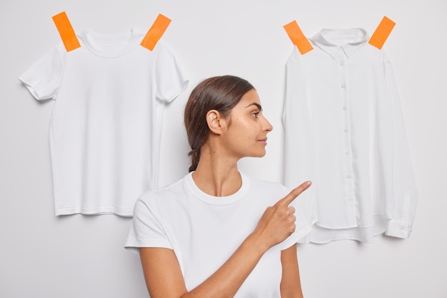 woman points finger on white shirt plastered to wall suggests outfit to wear focused away grabs your attention to clothes.