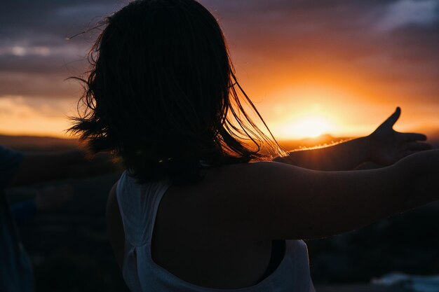 山の夕日を指差す女性