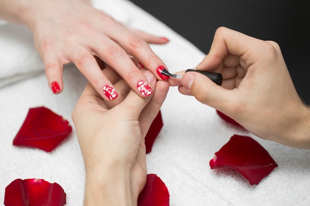 Woman polishes her nails with red nail polish in a beauty salon