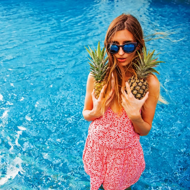 Woman at poolside holding two pineapples