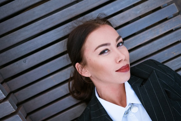 Woman portrait on a wooden background close-up. Beautiful young woman of Caucasian ethnicity, brunette with bright makeup and red lipstick on her lips in a business suit and white shirt