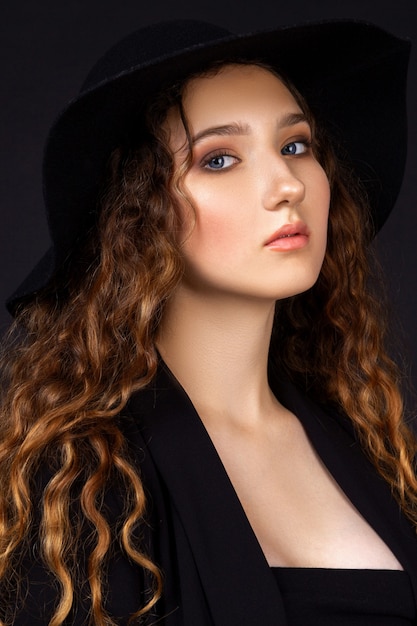 Woman posing over black wall, dressed in underwear, jacket and hat