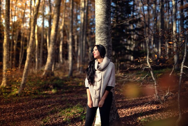 Photo woman posing by tree trunk in forest