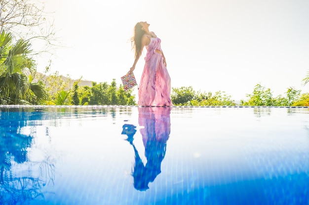 Woman posing next to an outdoor tropical pool with the image reflected on the water