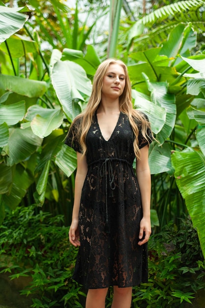 Женщина позирует в парео богемном летнем платье возле тропических деревьев