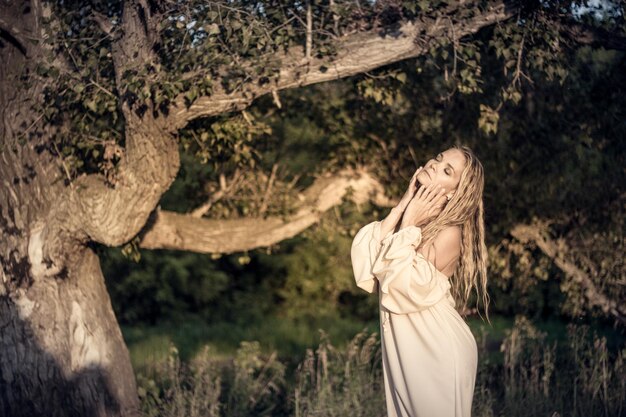 Foto donna che posa mentre è in piedi accanto ad un albero nella foresta