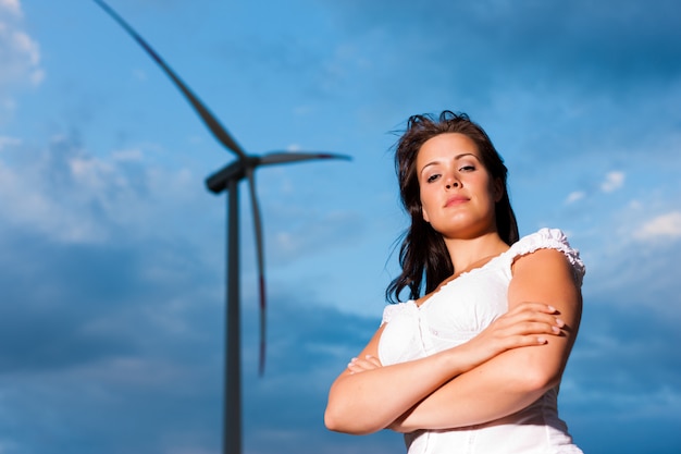 Woman posing with arms folded in front of windmill with cloudy sky in the background