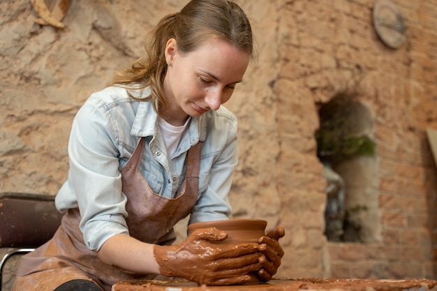 Donna vasaio che lavora al tornio da vasaio facendo un maestro di pentola di argilla che forma l'argilla con le sue mani creando un vaso in un'officina