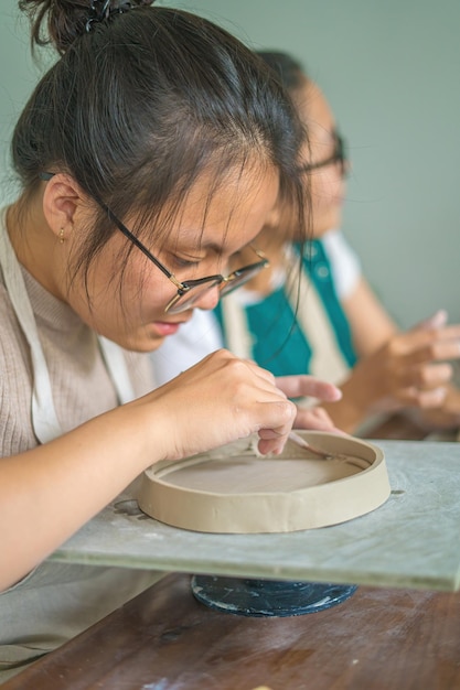 陶器ワーク ショップ アート コンセプトで粘土からセラミック ポットを作る陶芸家のホイールに取り組んでいる女性陶芸家フォーカス手若い女性粘土製品の部分を将来のセラミック製品に取り付ける陶器ワーク ショップ