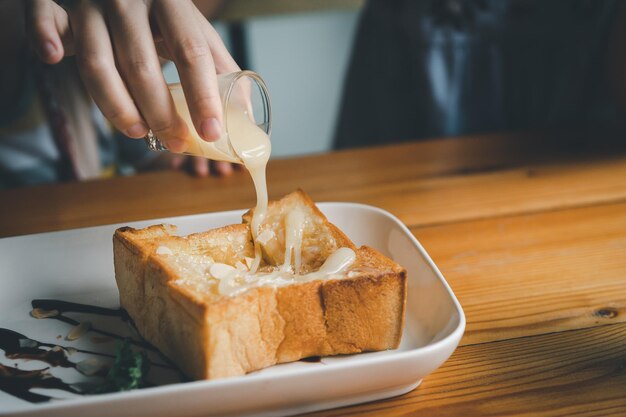 Woman pouring condensed milk on toast on the dining table woman
eating toast in the cafe restaurant food bakery concept