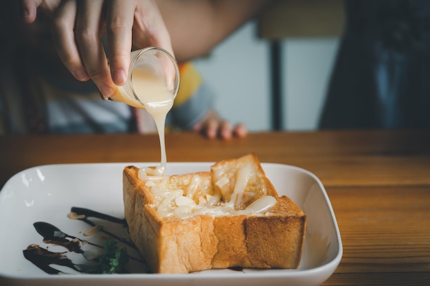 Woman pouring condensed milk on toast on the dining table woman\
eating toast in the cafe restaurant food bakery concept