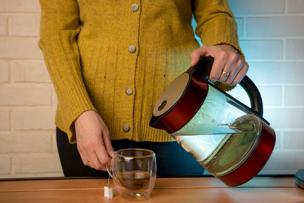 Photo woman pouring hot water from a kettle into a clear glass mug