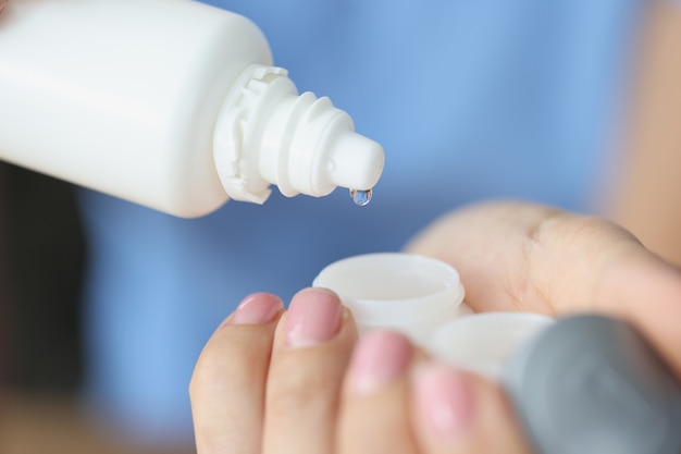 Woman pouring lens solution from bottle into plastic container closeup daily contact lens care