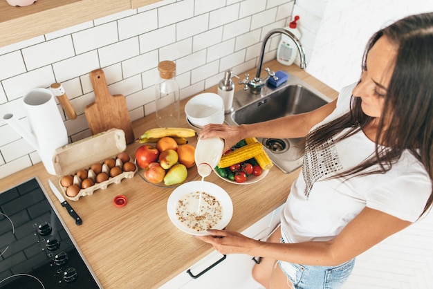 Woman pouring milk in plate with oak flakes.