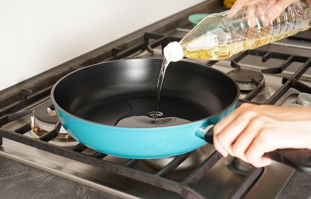 Woman pouring oil from bottle into pan in kitchen Closeup