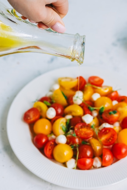 Woman pouring olive oil to fresh healthy salad with cherry tomatoes and mozzarella.