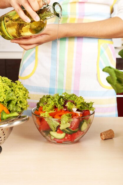 Woman pouring olive oil in vegetable salad in kitchen