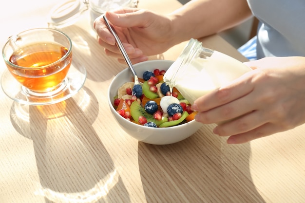 Woman pouring tasty yogurt onto fruits in bowl at table