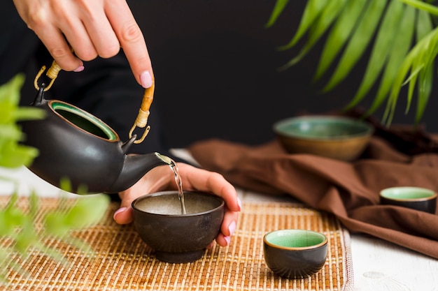 Tè di versamento della donna in tazza con la teiera