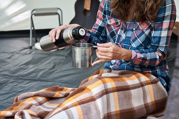 キャンプテントの魔法瓶からお茶を注ぐ女性