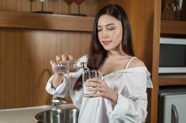 Woman pouring water from bottle to glass in kitchen