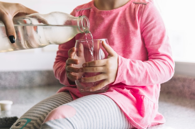 Woman pouring water in glass for her daughter