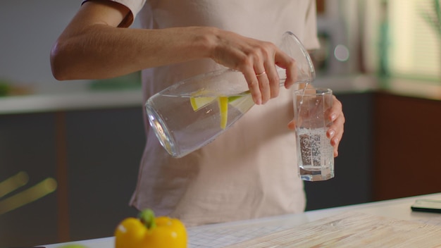Woman pouring water into glass from jug at home Girl drinking water on kitchen