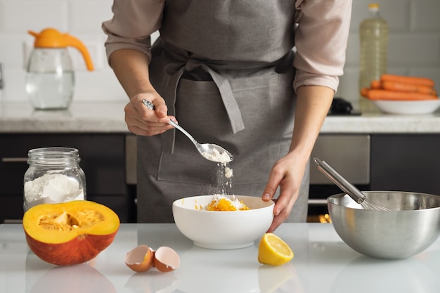 A woman pours flour into a bowl for making pumpkin pie