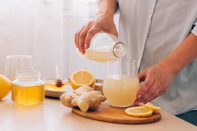 Woman pours freshly prepared drink from ginger root lemon honey into glass Health tea antioxidant