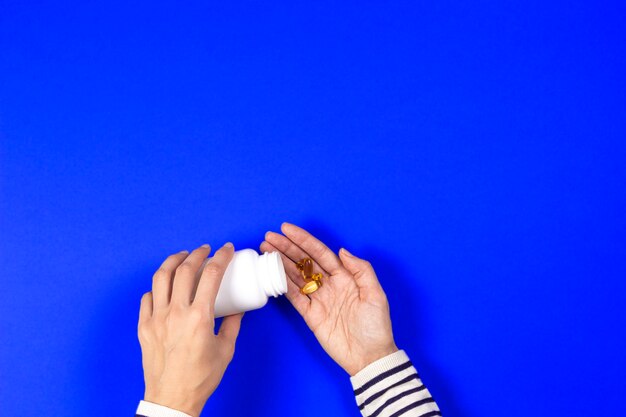 Woman pours from white bottle yellow capsules of omega 3 on blue background