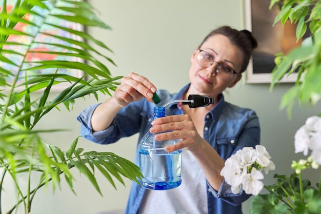 女性はスプレーボトルに液体ミネラル肥料を注ぎ、植物の葉を肥やします。屋内鉢植えの栽培と世話。趣味とレジャー、家庭菜園観葉植物、都会のジャングルのコンセプト