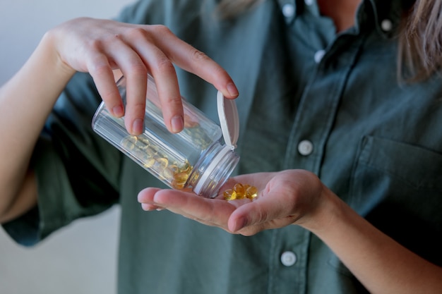 Woman pours out of a jar pills with cod liver oil. Side view