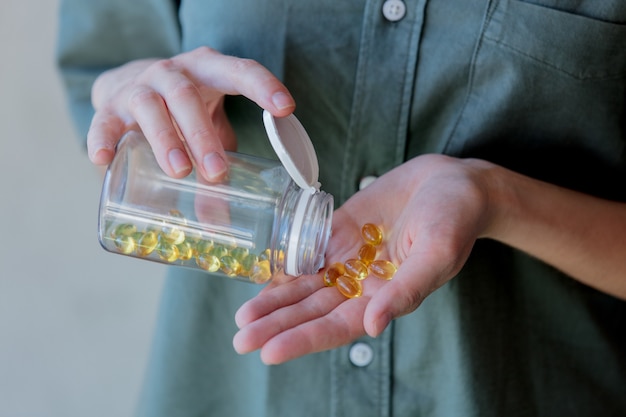 Woman pours out of a jar pills with cod liver oil. Side view