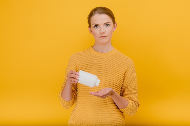 Photo woman pours pills from a tube with vitamins on her palm  having doubtful expression